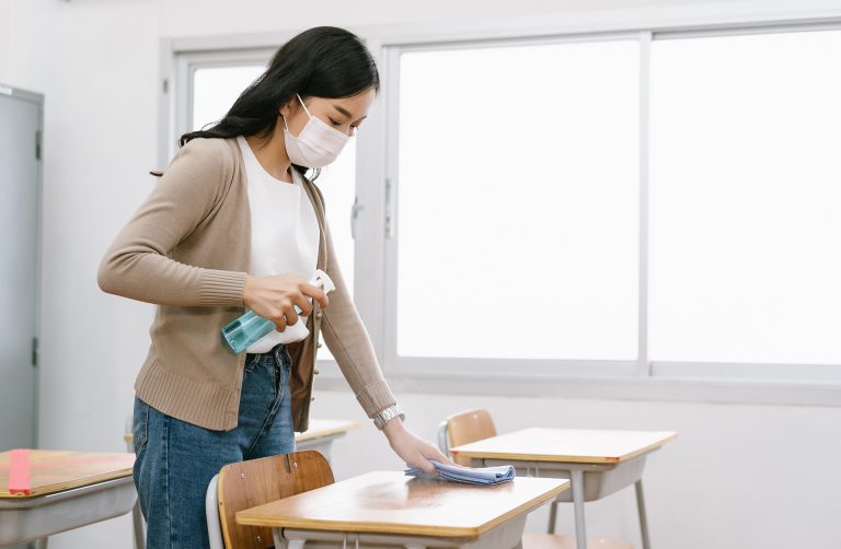 Young Asian female Teacher in a medical mask cleans up the desk